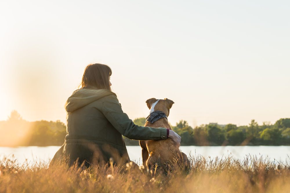 woman sitting by lake with dog